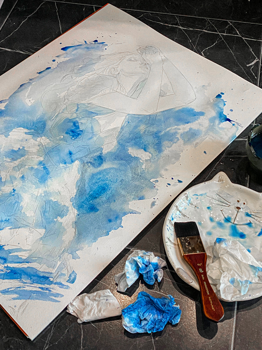 Artistic depiction of a person with blue and white watercolor on paper, with a brush and paint on a black surface.