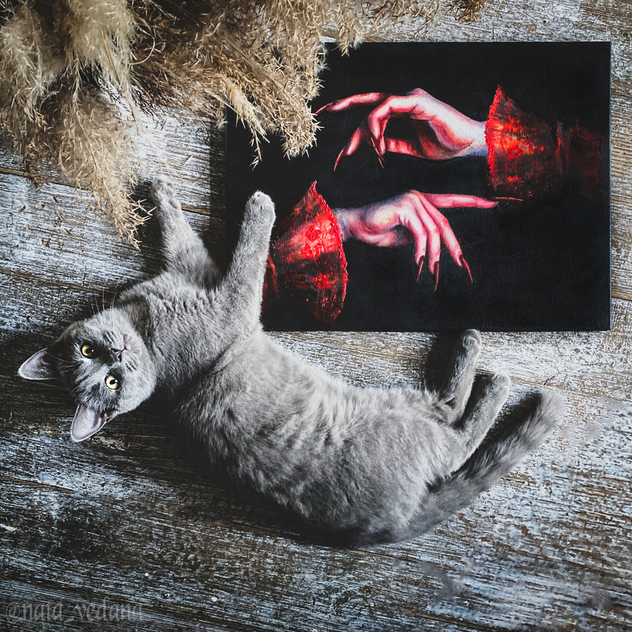 Gray cat lying on a wooden surface with a painting of hands in the background