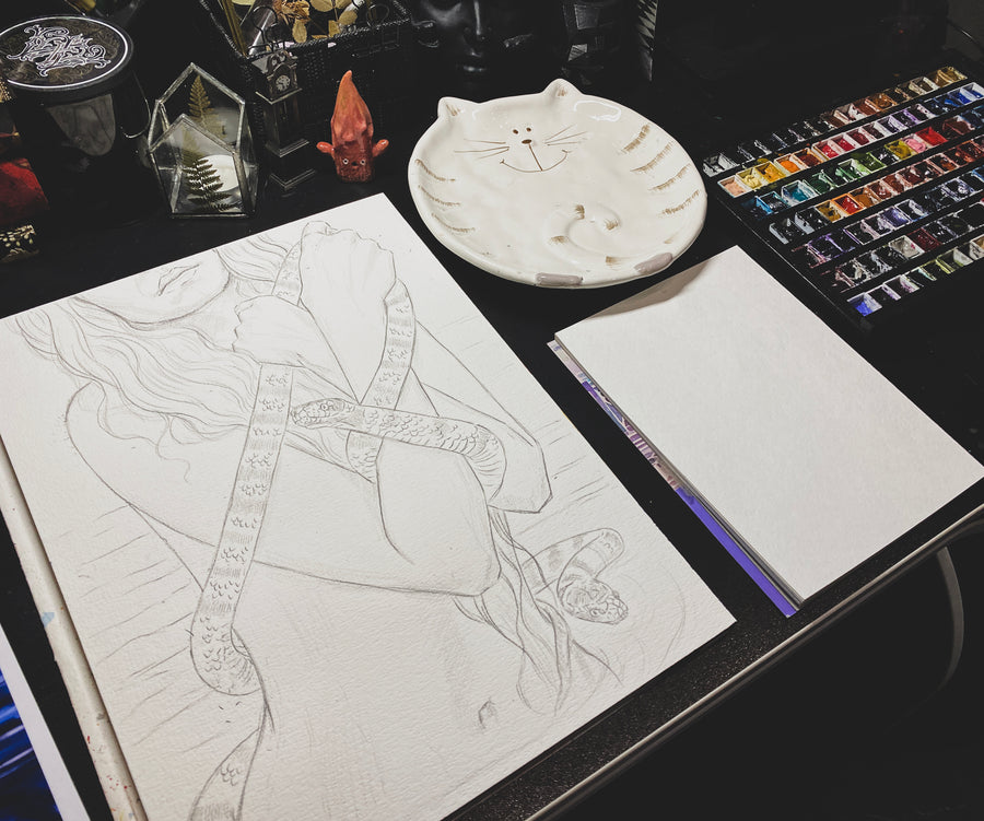 Artistic workspace with a drawing of a character, watercolor paints, and a palette on a dark surface.